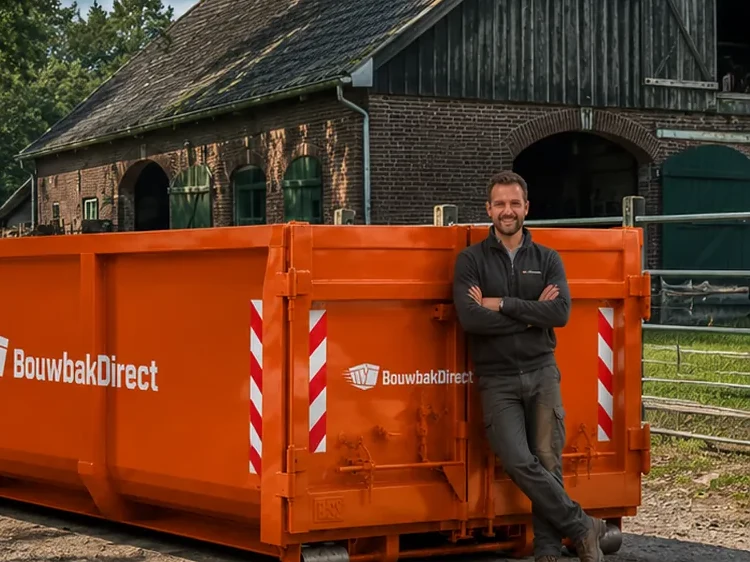Grote oranje afzetcontainer van BouwbakDirect bij een boerderij, met een medewerker ernaast