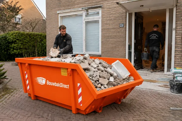 Afvalcontainer voor een woning waarin puin van verwijderde tegels wordt gegooid