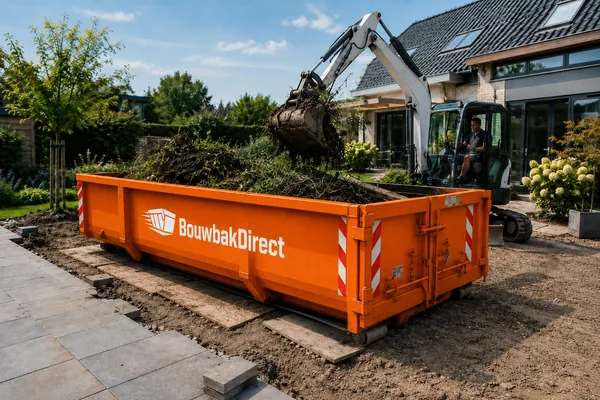 Minigraver laadt takken en wortels in een oranje afvalcontainer tijdens het opknappen van een tuin