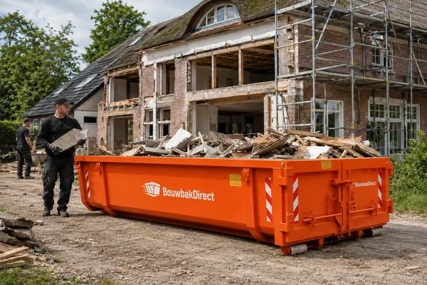 Oranje afvalcontainer van BouwbakDirect vol sloophout voor een woning in verbouwing, met steigers
